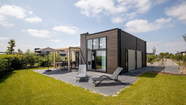 Ein modernes Haus mit Terrasse, zwei Loungestühlen und einer Glastür zu einem Innenbereich.