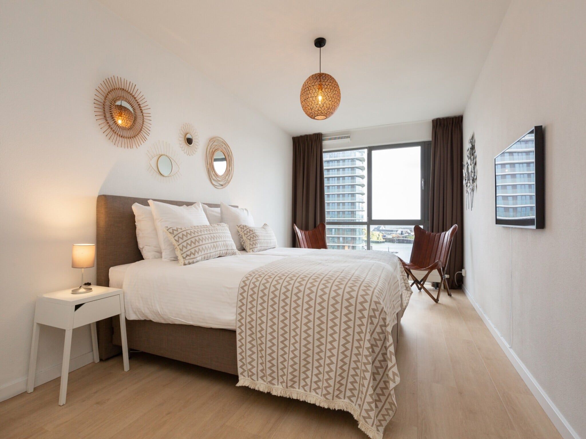 A modern bedroom with a large bed, bedside table, and a hanging light fixture.