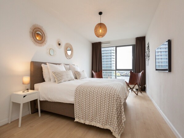 A modern bedroom with a large bed, bedside table, and a hanging light fixture.