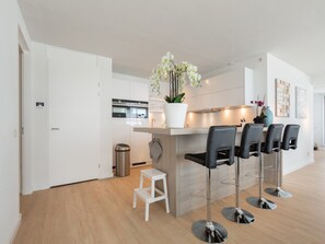 A modern kitchen with white cabinets, a stainless steel trash bin, and a white stool.