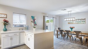 A modern kitchen with white cabinetry, a central island, and a dining area with a wooden table and metal chairs. - Private Pool + Outdoor Oasis • 5mins to Old Town | Indianola Oasis by AvantStay (Scottsdale)