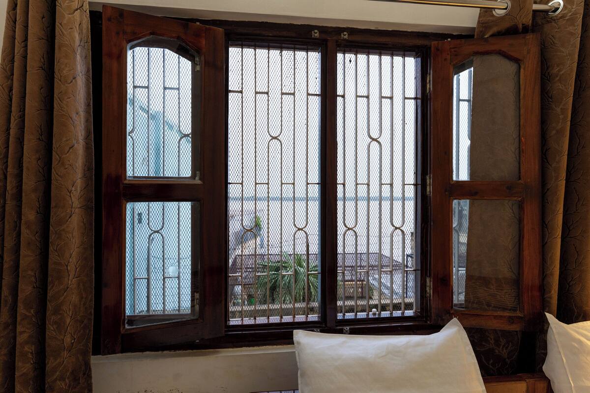 A room with a large window featuring metal bars, a wooden door, and a view of a building outside.