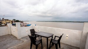 A terrace with a table and chairs overlooking a river. - Varanasi Rest House  (Varanasi)