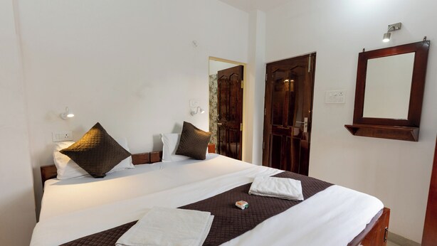 A neatly made bed with pillows, a bedside table, and a mirror on the wall. - Varanasi Rest House  (Varanasi)