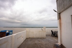 Una terraza en la azotea con vista a una gran masa de agua, un muro de concreto y una mesa con sillas.