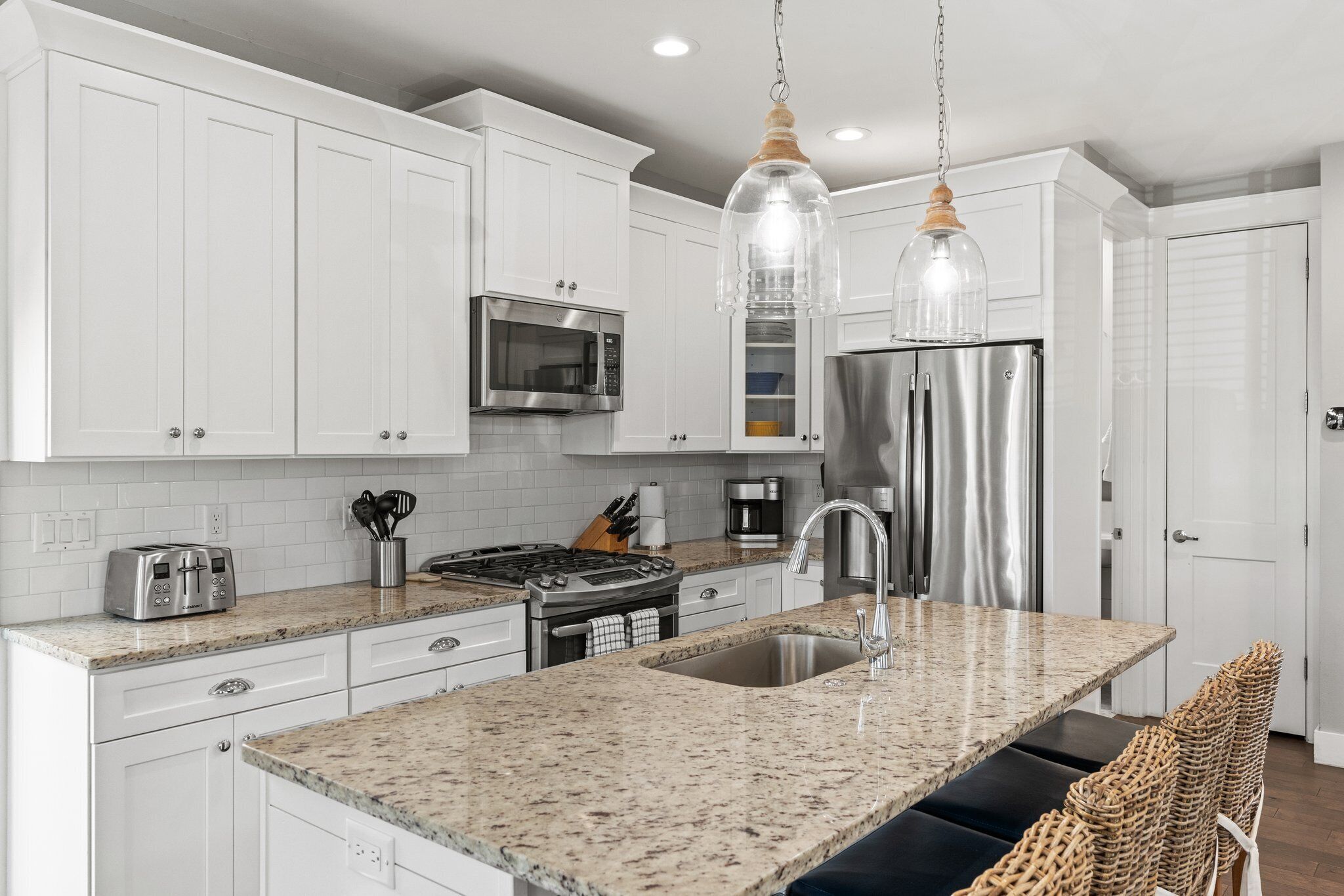 A modern kitchen with white cabinets, stainless steel appliances, granite countertops, and a central island with seating.