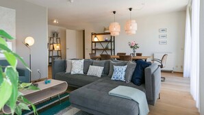 A modern living room with a grey sectional sofa, a wooden coffee table, and a dining area with a wooden table and chairs. - Apartment in Den Haag with sea beach (Den Haag)