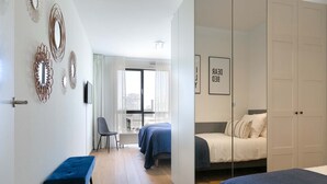 A modern hotel room with a large bed, a smaller bed, a desk, and a chair. There are decorative wall mirrors and a bench. - Apartment in Den Haag with sea beach (Den Haag)