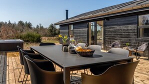 Un área de comedor al aire libre moderna con una terraza de madera, una mesa grande y sillas.