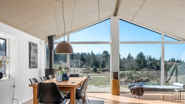 Un comedor moderno con una mesa y sillas de madera, ventanas amplias que ofrecen vistas al exterior y un techo con diseño de listones de madera.