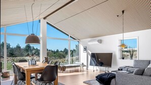 Una sala de estar moderna con un televisor grande, un comedor con mesa y sillas de madera, y vistas al exterior.