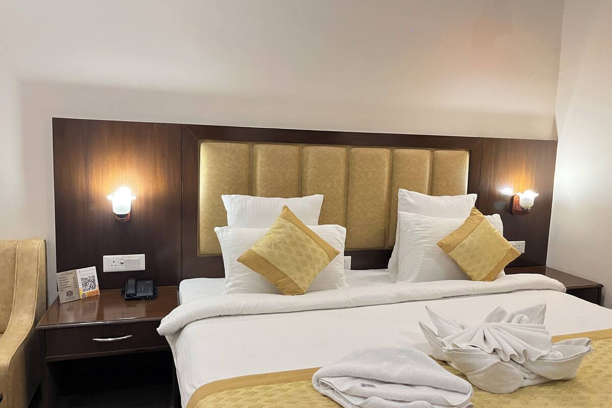 A hotel room with a large bed, two bedside tables, a nightstand, and a wall-mounted light fixture.