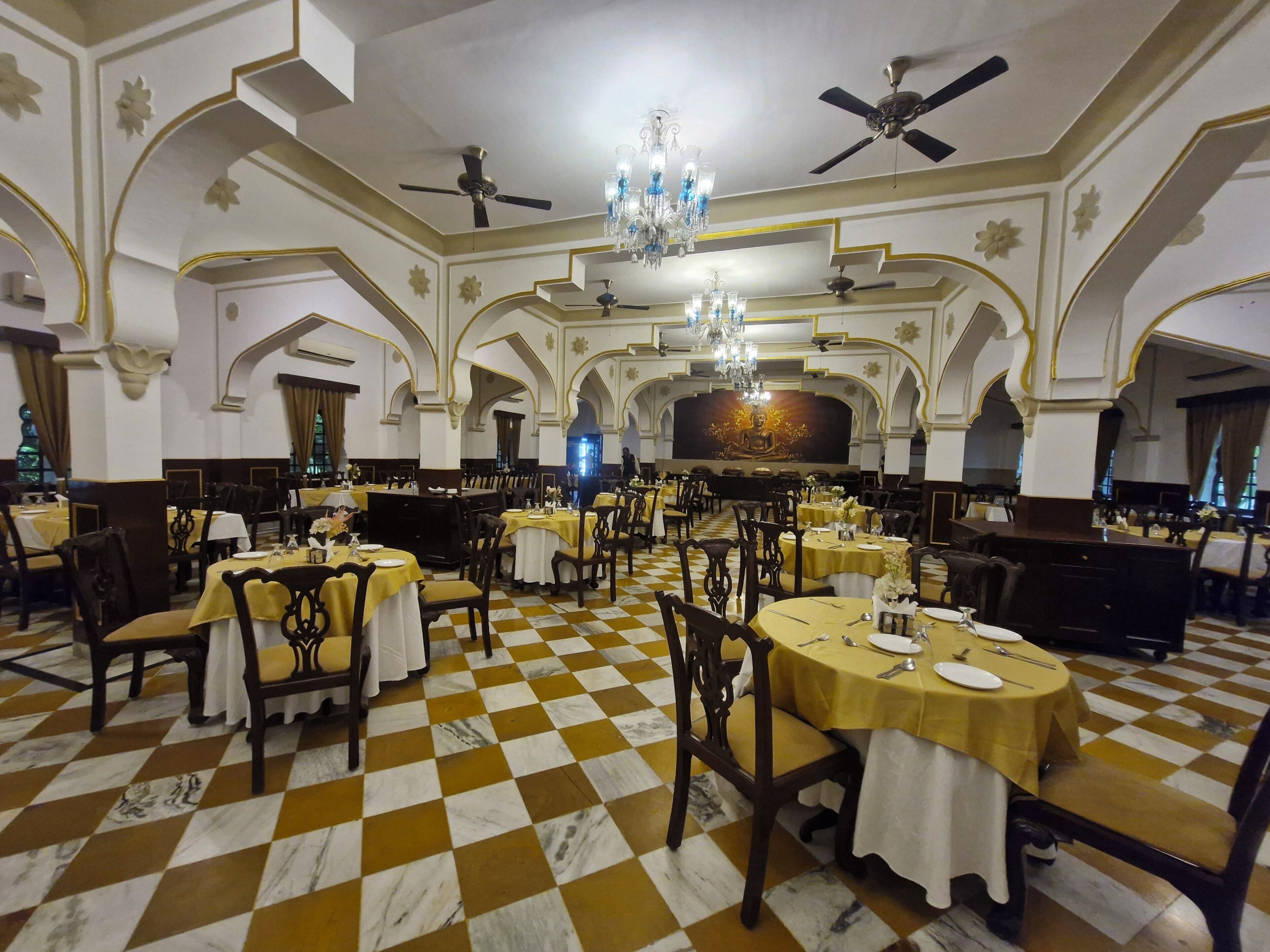 A large dining hall with checkered flooring, chandeliers, and ornate ceiling designs.
