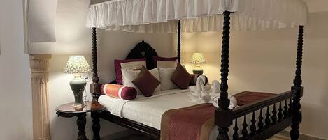A four-poster canopy bed with a checkered floor, two bedside tables with lamps, and a decorative headboard.