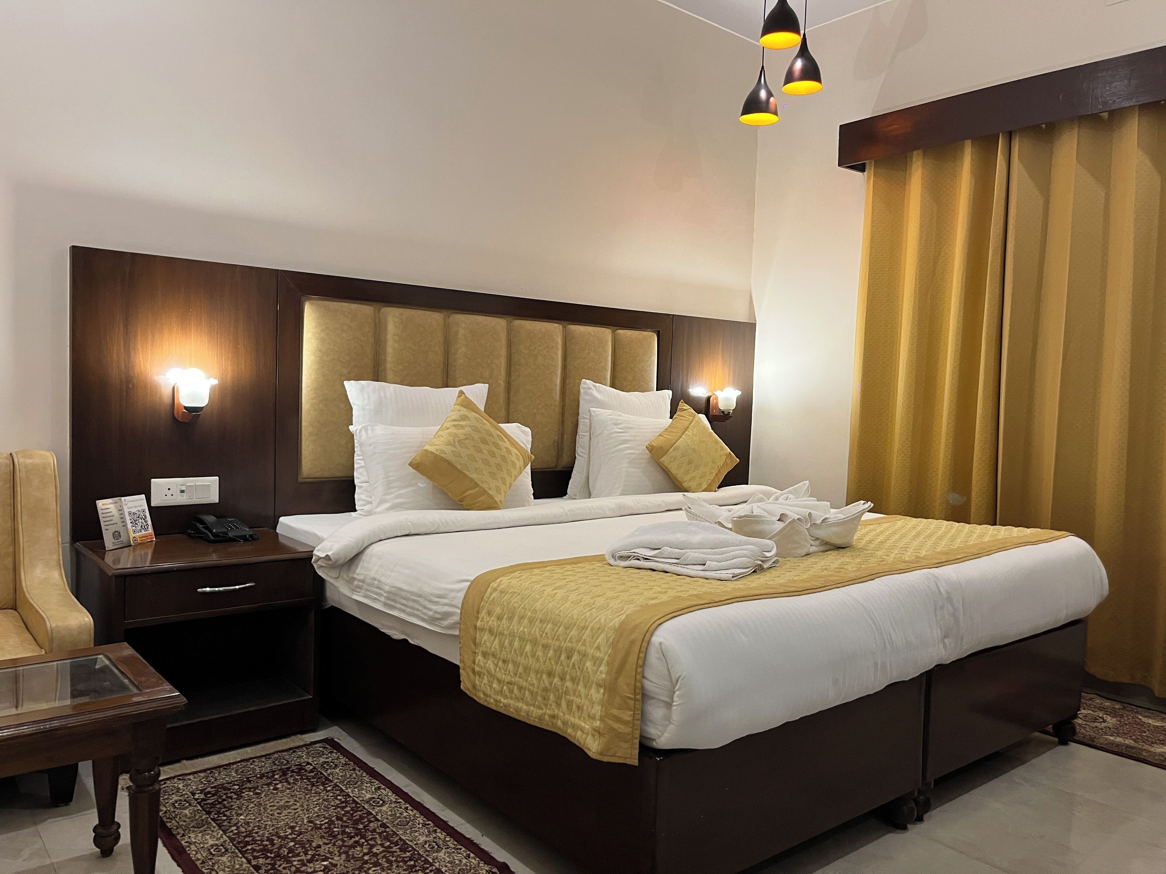 Ein Hotelzimmer mit einem großen Bett, einem Nachttisch mit Lampe, einem Sessel und einem kleinen Teppich.