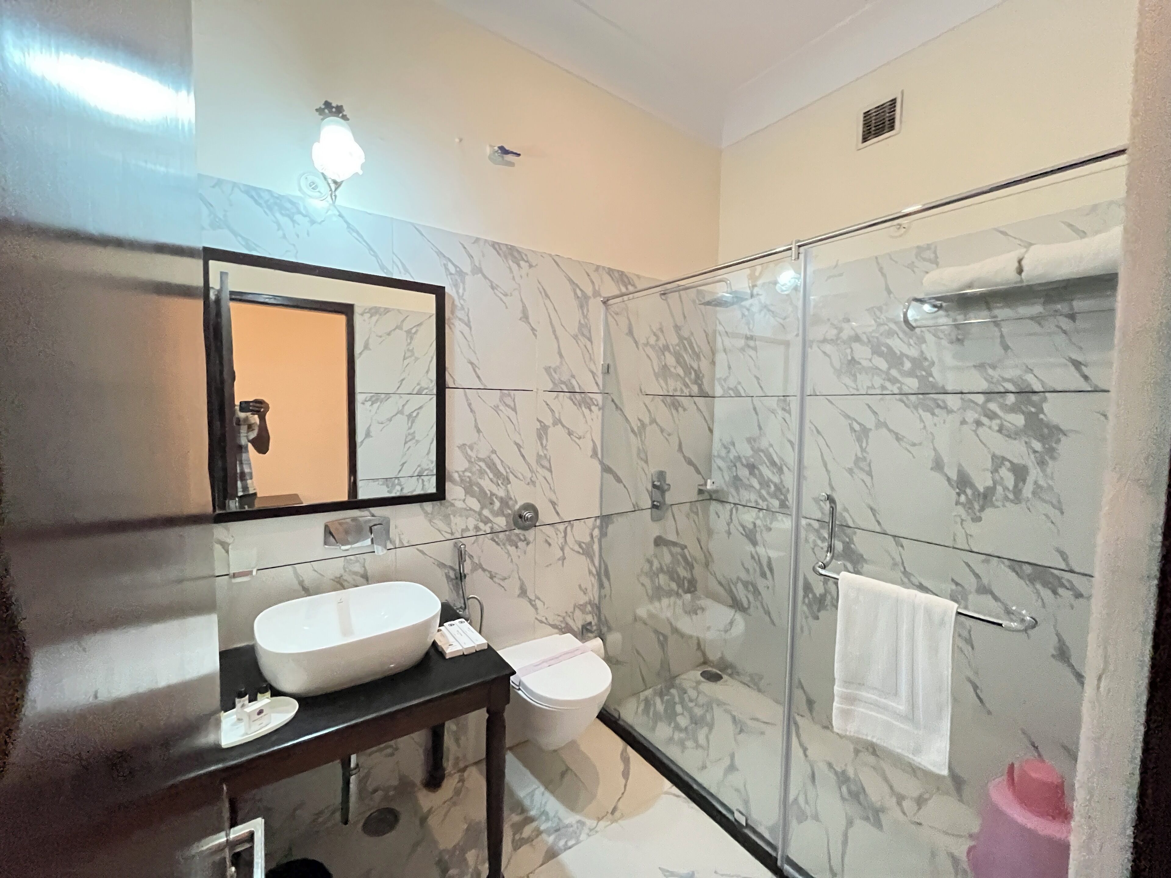 A bathroom with a marble wall, a glass shower enclosure, a white sink, and a toilet.