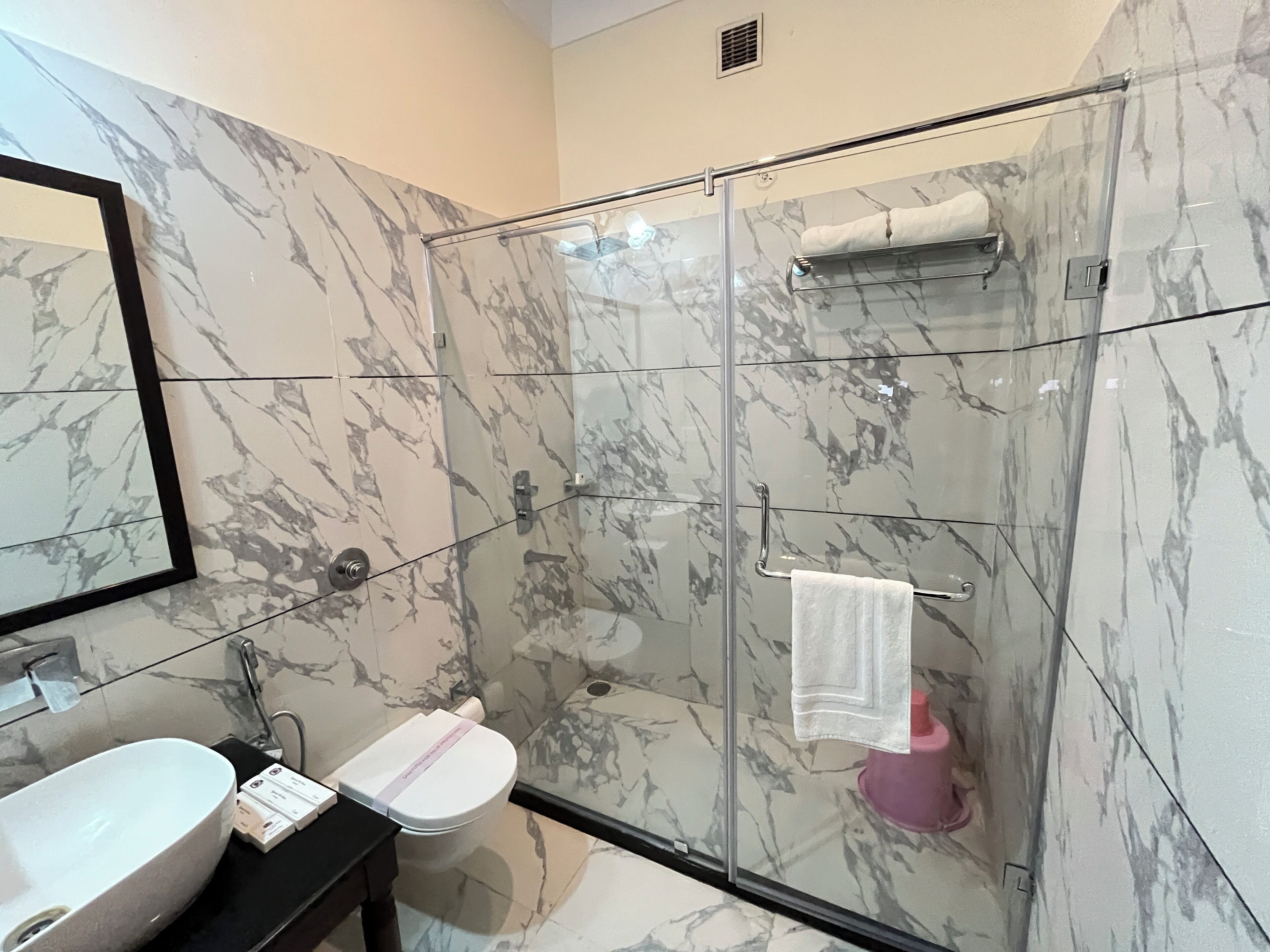 Un baño moderno con ducha envuelta en vidrio, un lavamanos blanco y un pared revestido de mármol.