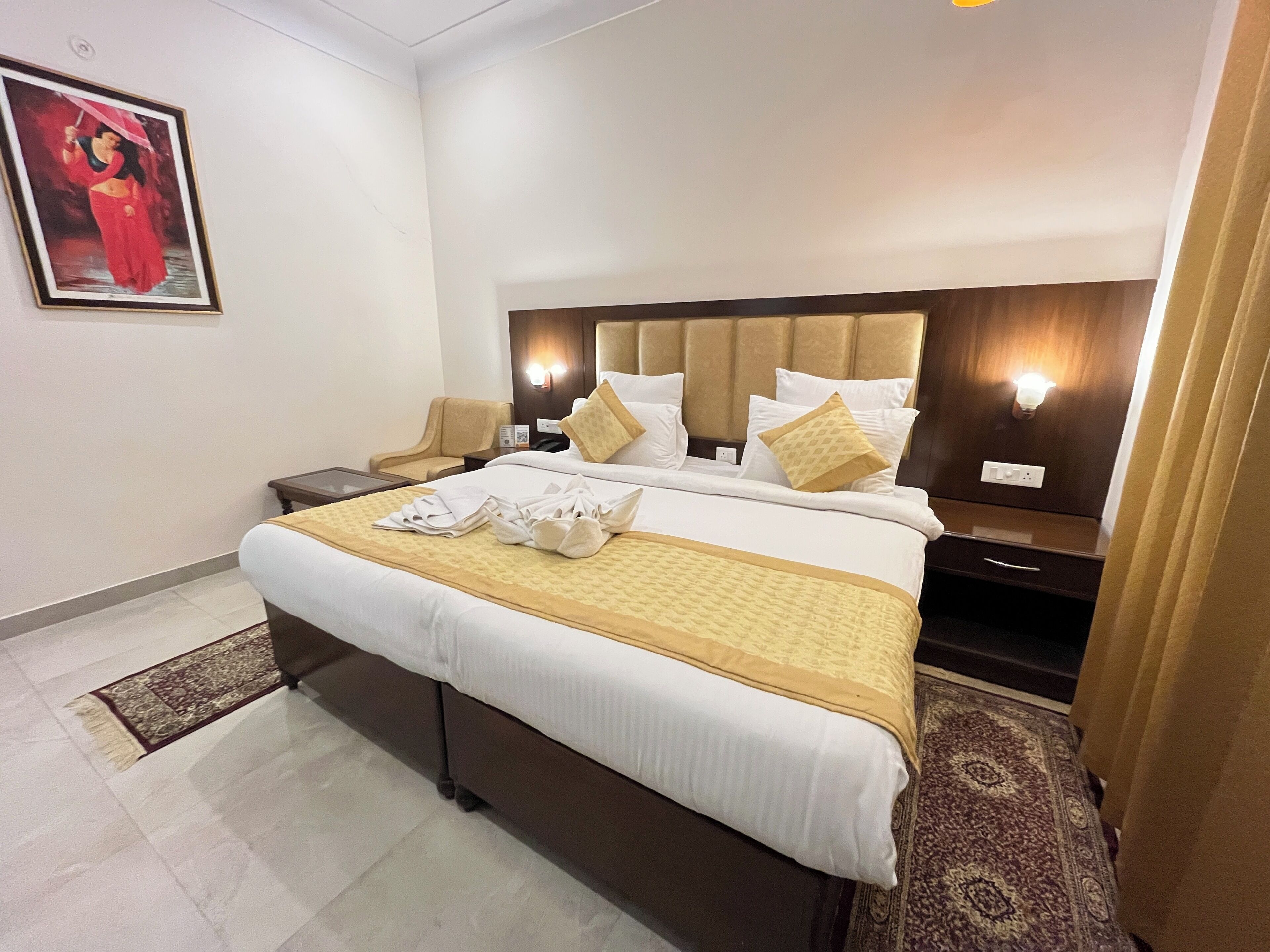 Habitación de hotel con una cama grande, una mesita de noche, una silla, una lámpara de pared y un cuadro enmarcado.