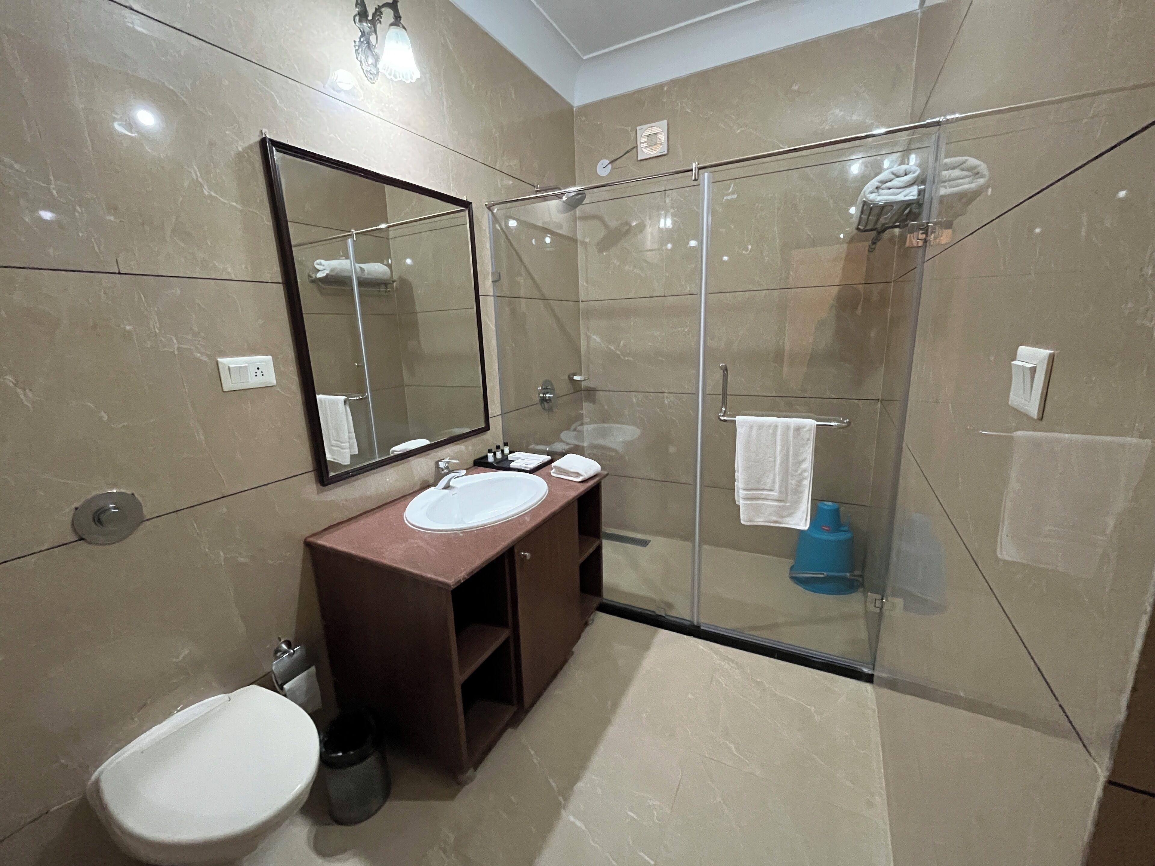 A modern bathroom with a glass-enclosed shower, a marble-tiled wall, a white sink, and a large mirror.