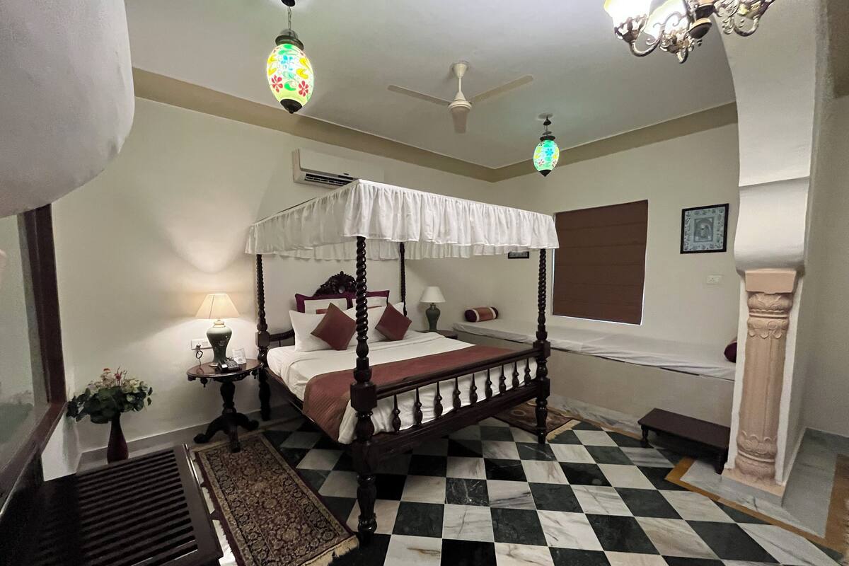 A four-poster bed with a canopy, a checkered floor, a chandelier, and a ceiling fan.