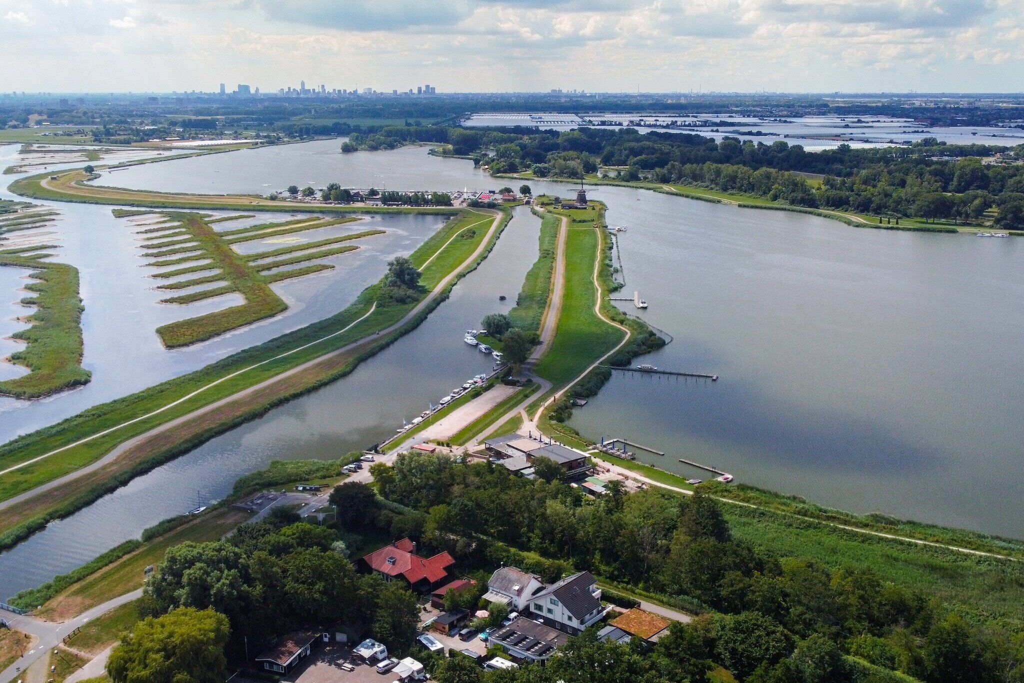 An aerial view of a riverside area with a lock system, a bridge, and a city skyline in the distance.