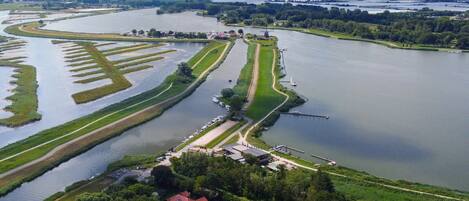 An aerial view of a riverside area with a lock system, a bridge, and a city skyline in the distance.
