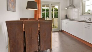 A modern kitchen with white cabinets, a large window, and a dining area with brown chairs. - Bungalow in South Holland with Private Jetty (Simonshaven)