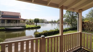 A covered porch with a view of a lake, a house with a red roof, and a dock. - Bungalow in South Holland with Private Jetty (Simonshaven)
