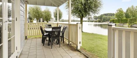 A covered patio with a table and chairs, overlooking a lake.
