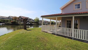 A house with a covered porch, a river, and a tree in the foreground. - Bungalow by Water near Rotterdam with Sauna (Simonshaven)