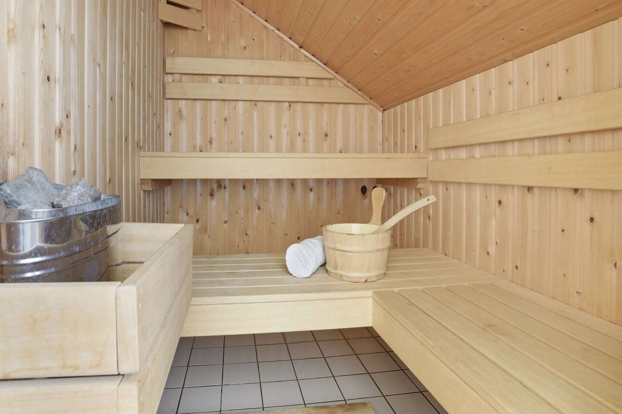 A wooden sauna with benches, a metal container, and a wooden bucket with a ladle.