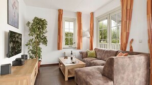 A living room with a wooden desk, a sofa, a coffee table, a potted plant, and a window with curtains. - Bungalow by Water near Rotterdam with Sauna (Simonshaven)