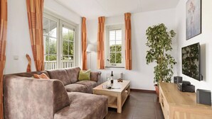 A living room with a sofa, a coffee table, a lamp, a potted plant, and a TV on the wall. - Bungalow by Water near Rotterdam (Simonshaven)