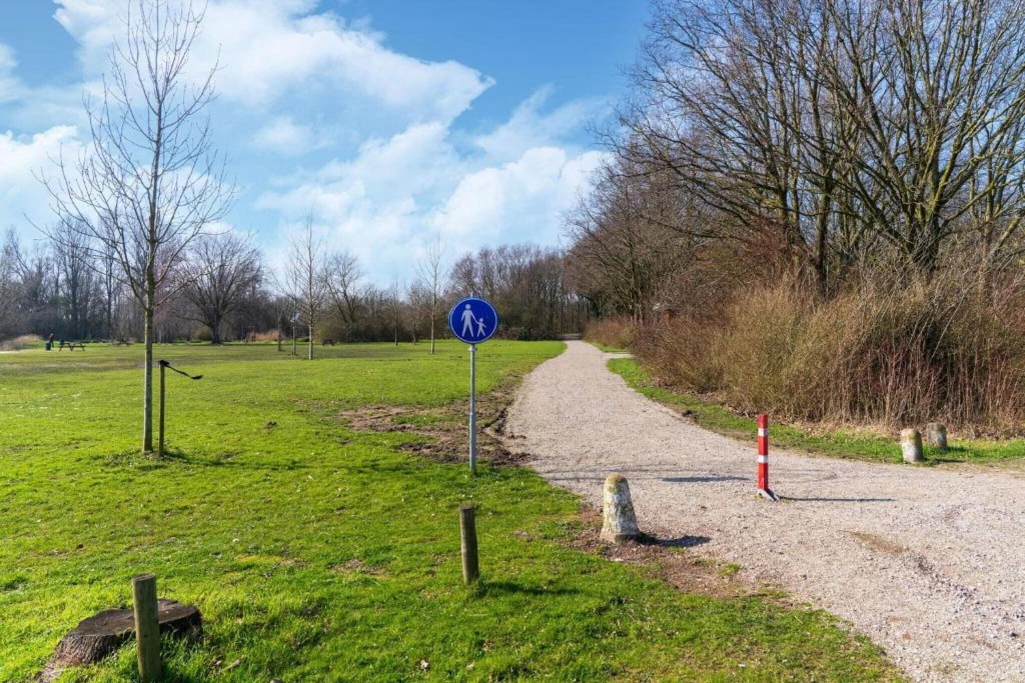 A gravel path leading through a park with a blue pedestrian sign.