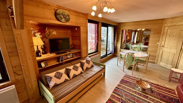 A cozy cabin interior with a wooden sofa, a television, and a dining area with a table and chairs. - L'Oise 405 - Le Mont Dore 6pers (Mont-Dore)