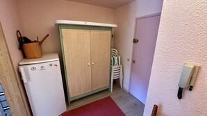 A compact kitchen with a white refrigerator, a wooden cabinet with a green top, and a red rug on the floor. - L'Oise 405 - Le Mont Dore 6pers (Mont-Dore)