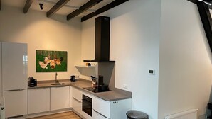 Une cuisine moderne avec des armoires blanches, une poubelle en acier inoxydable, une hotte noire et un tableau représentant des poulets accroché au mur.