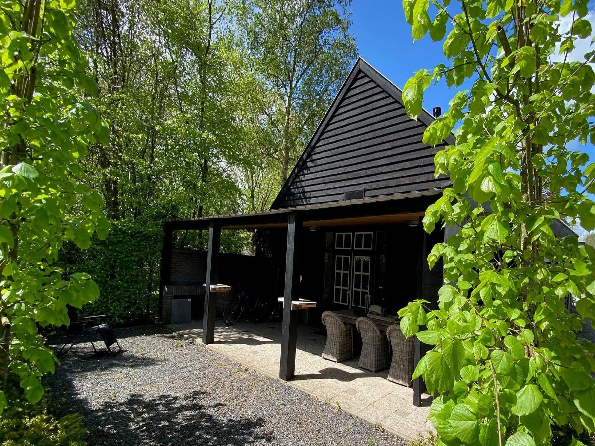 Une cabane en bois avec un toit en pente, entourée d’arbres et bordée d’un chemin de gravier.