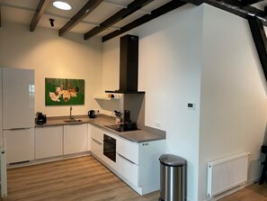 A modern kitchen with white cabinets, a stainless steel sink, and a black range hood. - Apartment in Wageningen near Rhine River (Elst)