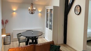 Une pièce chaleureuse avec une table ronde, un canapé, un lustre, une armoire et une horloge au mur.