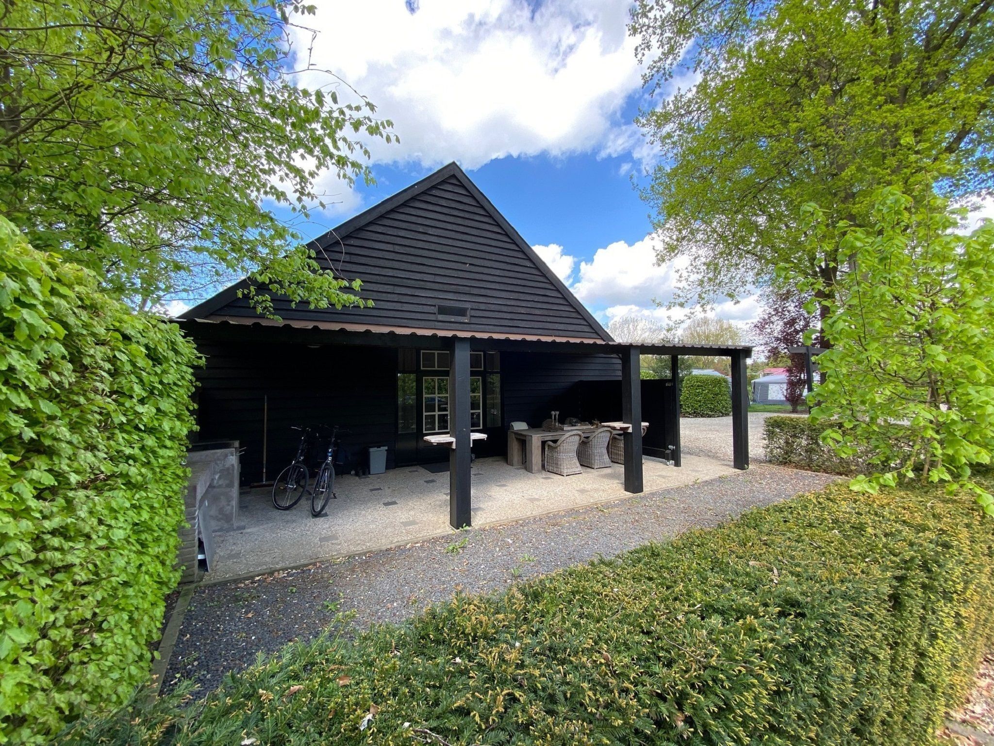 A black building with a covered patio area, a bicycle, and a gravel path.