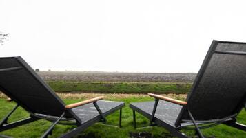 Two black lounge chairs with wooden armrests facing a vast, open field.