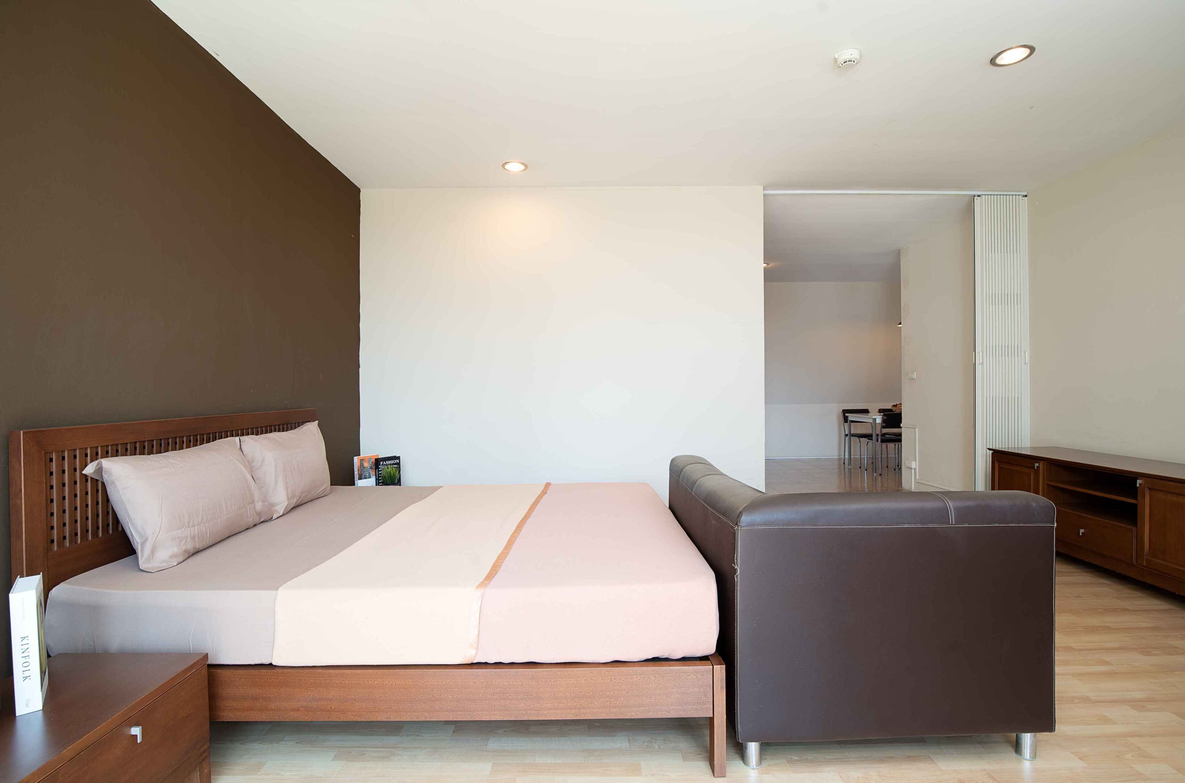 Una camera da letto moderna con un letto in legno, un comodino, un poggiapiedi in pelle marrone e vista sull'area pranzo adiacente.