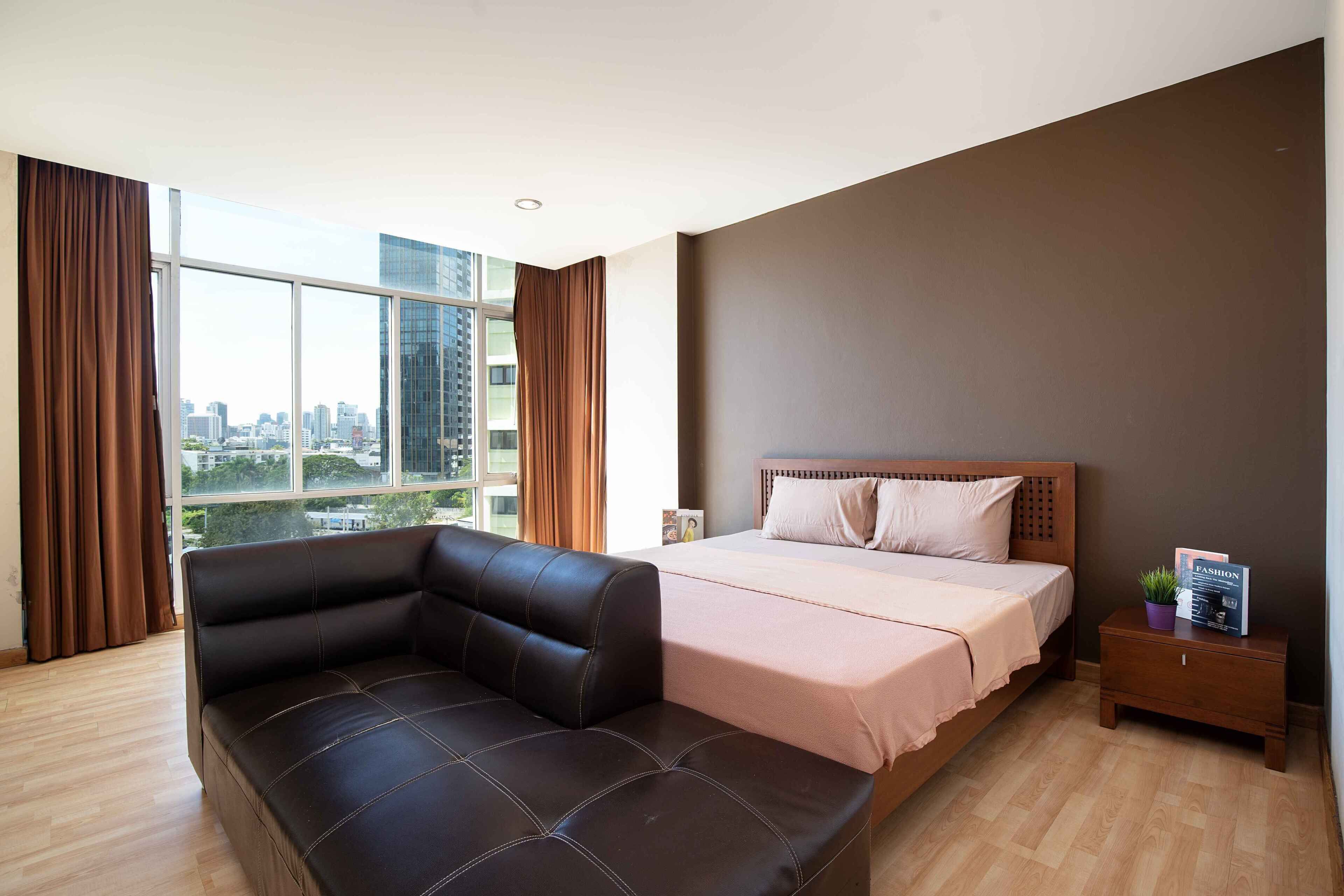A modern bedroom with a large window, a bed, a leather sofa, and a nightstand.