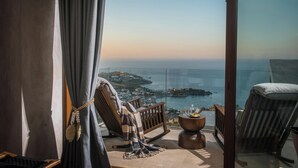 Un balcón con vistas al mar, una silla de madera, una mesita redonda y una silla a rayas.