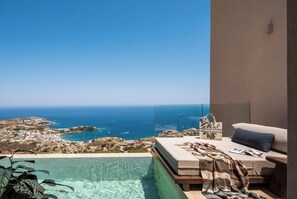 Un balcon avec vue sur la mer et sur la ville, un canapé et une petite table sur laquelle est posé un sac à main.