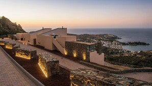 Un hotel costero de diseño moderno, con un camino de piedra que lleva a la playa, vistas al mar y un pueblo a lo lejos.