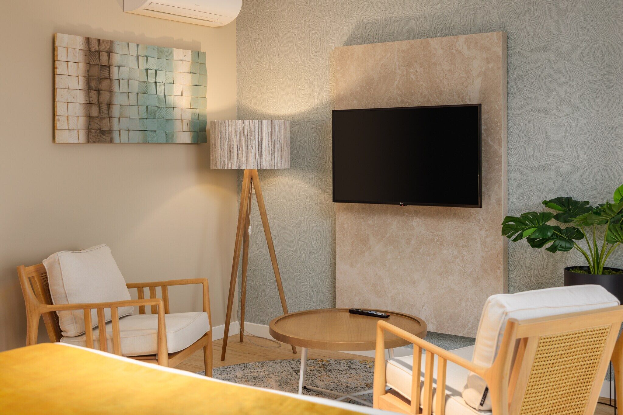A modern living room with a flat-screen TV mounted on the wall, a standing lamp, and two wooden chairs.