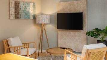 A modern living room with a flat-screen TV mounted on the wall, a standing lamp, and two wooden chairs.