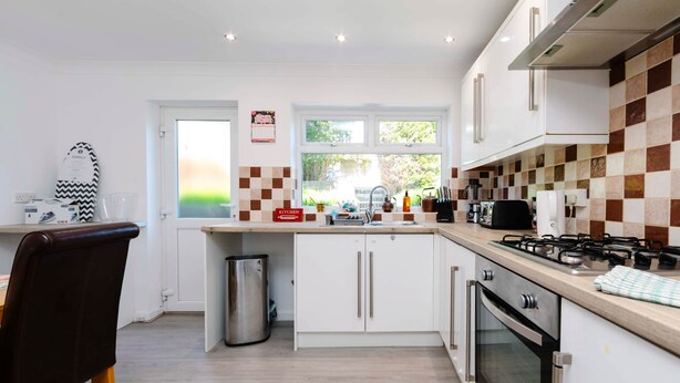 A modern kitchen with white cabinets, a stainless steel range hood, and a window with a view of greenery. - Gilfach Cynon Cottage - Beacons & BikePark (Merthyr Tydfil)
